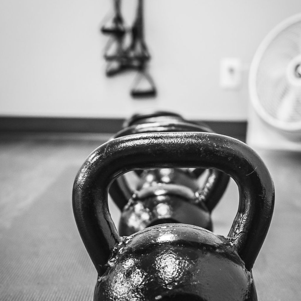 grayscale photo of kettlebell weights on the floor with strength straps in behind